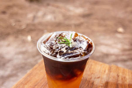 Iced coffee with ice cubes and rosemary on wooden table.の写真素材