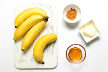 Ingredient for fried bananas with honey cinnamon butter sauce; Cavendish bananas, cinnamon, butter and honey. Top view on white table background. Make this easy banana dessert recipe.の写真素材