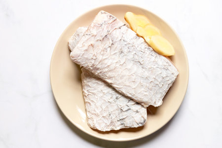 Fresh sea bass fillet with ginger sliced on dish, top view.