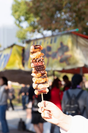 Woman hand holding grilled octopus skewer, ready to eat. Traditional food stall in Japan.