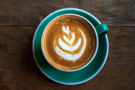 Cup of coffee with latte art on wooden table with morning sunlight through from window. Beautiful morning.の写真素材