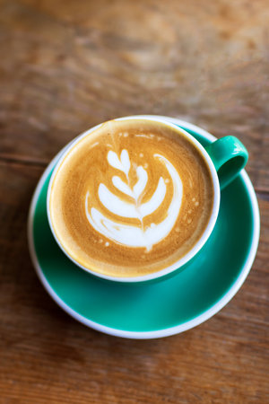Cup of coffee with latte art on wooden table with morning sunlight through from window. Beautiful morning.の写真素材