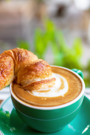 Cup of coffee with latte art with croissants on wooden table and morning sunlight with shadow through from window. Beautiful meal with warm sunlight.の写真素材