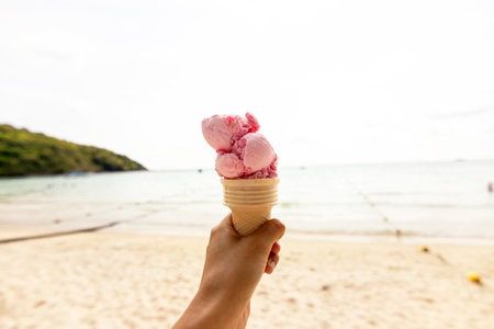 Hand holding ice cream cone on the beach in summer day.の写真素材