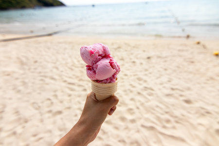 Hand holding ice cream cone on the beach in summer day.