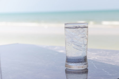 Glass of water on the table with sea and sand beach background.の写真素材
