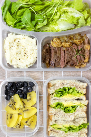 Set of lunch boxes with tasty food. Top view of lunch box with sandwiches, steak, salad, fruits and mashed potato.の写真素材