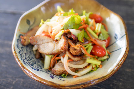Spicy salad with pork and vegetables in a bowl on wooden tableの写真素材
