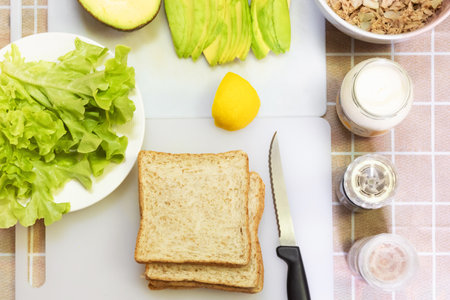 Preparing healthy sandwiches for breakfast ; whole wheat bread, tuna, egg, avocado and lettuce on white cutting board.の写真素材