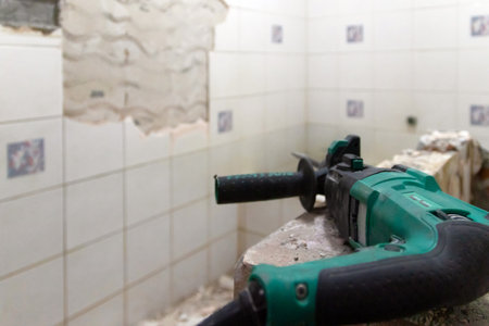 A construction worker is using a power tool to remove tiles from a bathroom wall.の写真素材