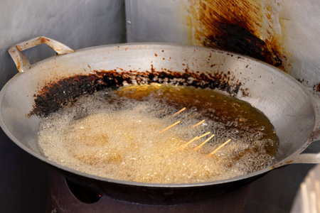 Large wok with hot oil and several skewers of food frying in it.
