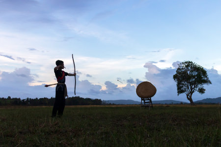 A man shooting an arrow at a target. The man is dressed in traditional clothing and the background...