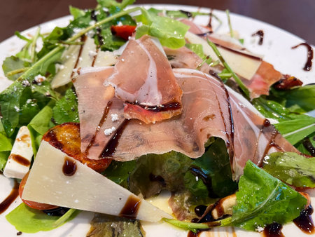 Fresh salad featuring greens, prosciutto, cheese, and a balsamic dressing for a delicious and healthy meal option.の写真素材