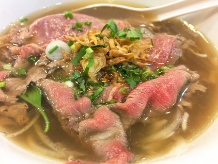 Delicious bowl of beef noodle soup garnished with fresh herbs and crispy onions, perfect for a...