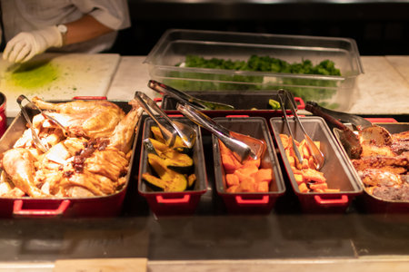 A vibrant array of delicious dishes at a buffet, showcasing a variety of meats and vegetables ready...