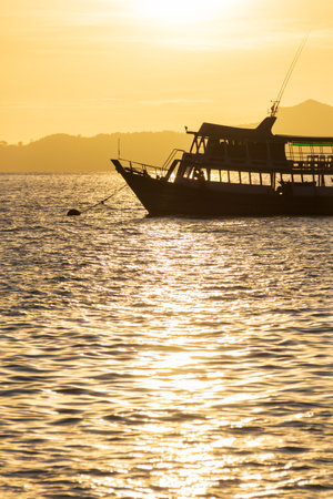 A tranquil sunset scene featuring a silhouette of a boat on shimmering water, creating a serene atmosphere.の写真素材