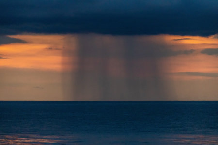 A serene sunset over a tranquil ocean, with dark clouds casting shadows and a distant light...