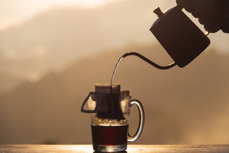 A serene scene of pouring hot water into a coffee bag, creating a rich brew against a beautiful mountain backdrop.の写真素材