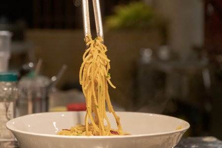 Chef holding tongs of Spaghetti aglio e olio; pasta with dried chili, garlic and olive oil.