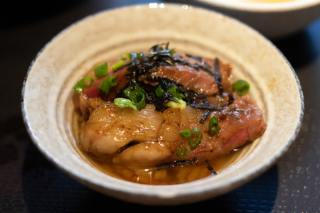 Delicious bowl of beef slices topped with green onions, served with soup.