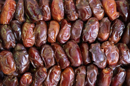 A close-up image of a pile of dates. The dates are a dark brown color and have a wrinkled texture.
