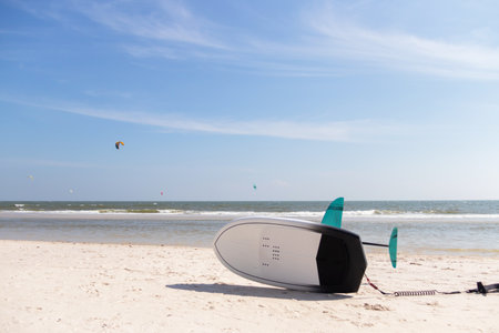 A tranquil beach scene featuring a surfboard laid on soft sand under a bright sunny sky with kites...