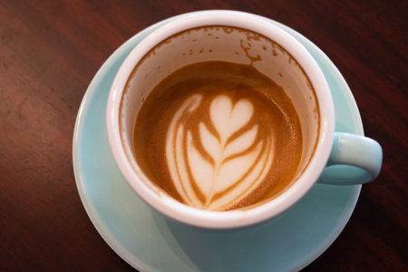 Cup of coffee with latte art on wooden table with soft sunlight. Perfect latte art on the bottom of cup.の写真素材