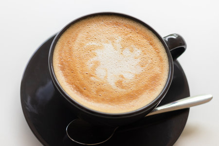 Hot coffee with milk in a black cup on white table.の写真素材