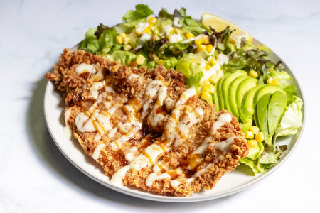 A delicious and meal. It includes a salad with lettuce, corn, tomatoes, and avocado. There is also a piece of deep fried chicken on top. The meal is drizzled with a light dressing.の写真素材