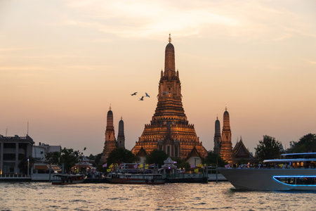 Wat Arun Ratchawararam Ratchawaramahawihan (Temple of Dawn) with a tourist on a cruise boat capturing a photo in a magical moment along the Chao Phraya river at twilight in Bangkok, Thailand.の写真素材