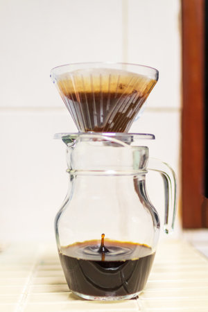 A freshly brewed cup of coffee. The coffee is being poured from a glass carafe into a glass cup. The coffee is dark and rich, and the crema is thick and creamy.の写真素材