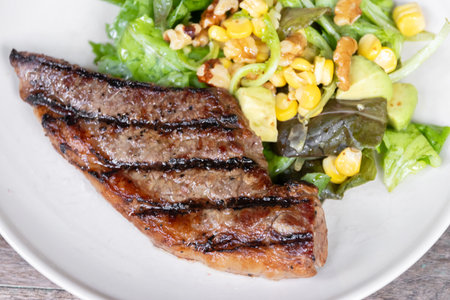 Grilled steak paired with a fresh salad featuring corn and greens, perfect for a delicious meal.の写真素材