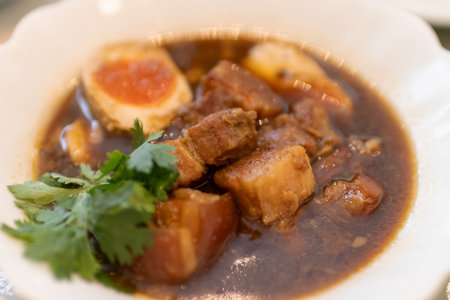 Delicious bowl of savory pork stew with eggs and fresh herbs garnishing.の写真素材