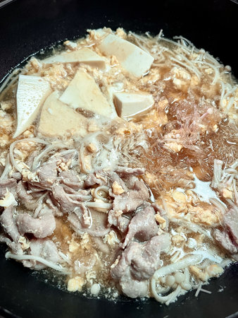 A tofu, thin sliced pork, mushroom and glass noodle hot pot simmering in savory broth with comforting steamの写真素材