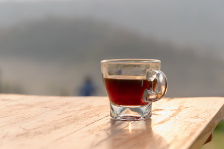 A glass cup of black coffee on wooden table with soft morning light and blurred outdoor backgroundの写真素材