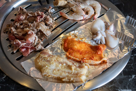 A grilled seafood and meat on tabletop grill, succulent shrimp, squid, marinated pork, sizzling flavorsの写真素材