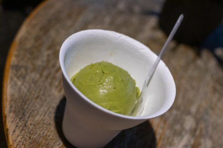 A green tea ice cream scoop in white cup with small spoon on wooden table, creamy dessert enjoymentの写真素材