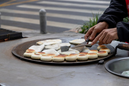A flat bread rounds and filled pancakes grilling on street griddle, hands flipping dough with spatula, warm golden crust, street food in China.の写真素材