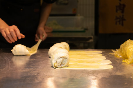 A Rolled pastry dough on stainless table with chef hands preparing (Guo Kui), crispy stuffed...