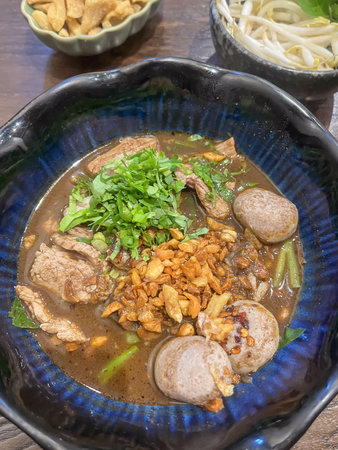 A beef noodle soup with herb garnish, fried garlic and meatball topping, rich broth and bean sprouts