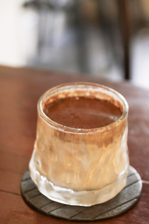 An iced chocolate drink in frosted glass on wooden coaster, creamy beverage with cocoa foamの写真素材