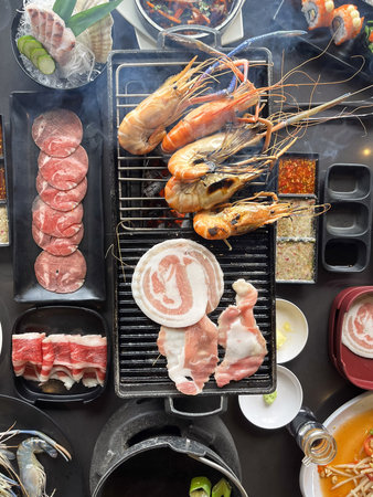 A grilled prawn and pork barbecue with sliced meat and dipping sauce, lively tabletop hotpot and seafood feastの写真素材