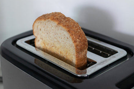 A whole grain bread slice in toaster warming with golden crust and cozy morning moodの写真素材