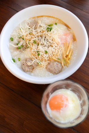 A rice porridge with meatball,soft boiled egg,crisp noodle and scallion garnish,comforting breakfast bowl with savory toppingsの写真素材