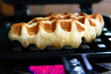 A golden waffle cooking on grill with melted butter and crisp edge, warm homemade breakfast scene with inviting textureの写真素材