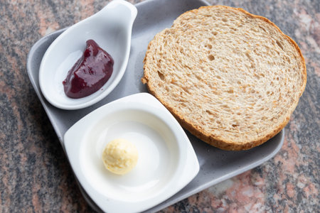 A whole wheat bread slice with butter ball and berry jam on ceramic plate, simple breakfast serving...
