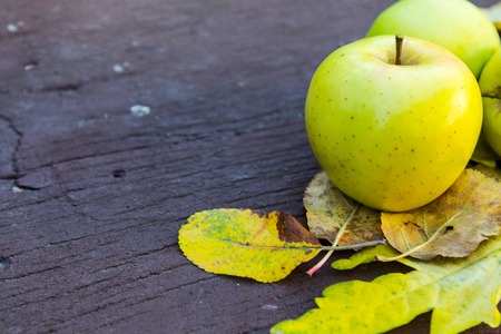Ripe green apples on a wooden background with yellow leaves.
