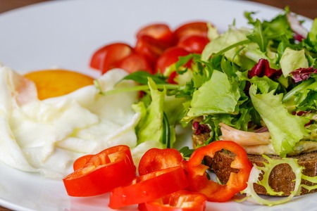 Breakfast fried egg, bread, tomatoes, hummus, pepper and rucola on wood table.