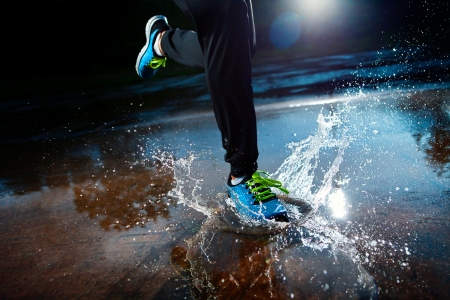 Single runner running in rain and making splash in puddle