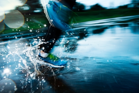 Single runner running in rain and making splash in puddle